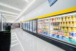Giant Tiger Boisbriand, Que., grocery aisle featuring refrigerated shelves stocked with various food items such as juices, dairy products, and packaged goods. The word “Épicerie” is displayed on the wall above the coolers, and black shopping baskets...