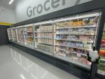 Giant Tiger Camrose, Alta., grocery aisle featuring refrigerated shelves stocked with various food items such as juices, dairy products, and packaged goods.  The word “Grocery” is displayed on the wall above the coolers. 